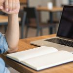 Ilustrasi seseorang berpikir di depan laptop dan buku catatan