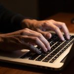 Ilustrasi tangan mengetik di keyboard laptop pada ruangan redup
