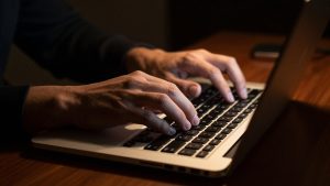 Ilustrasi tangan mengetik di keyboard laptop pada ruangan redup